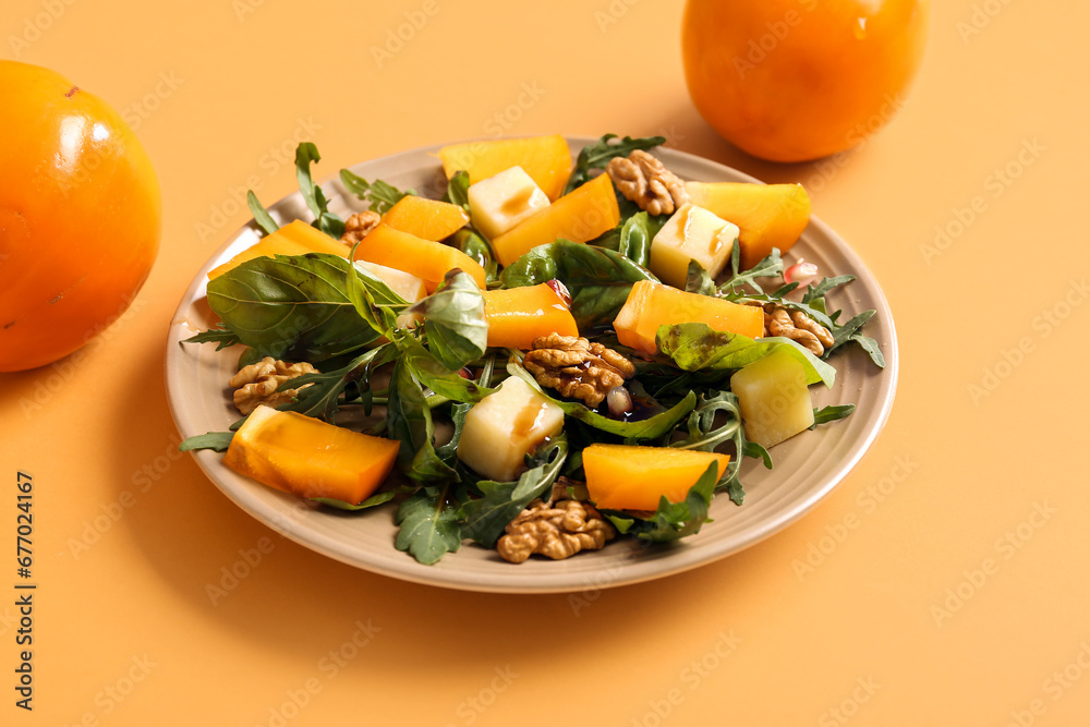 Plate of delicious salad with persimmon, pomegranate seeds and walnut on orange background