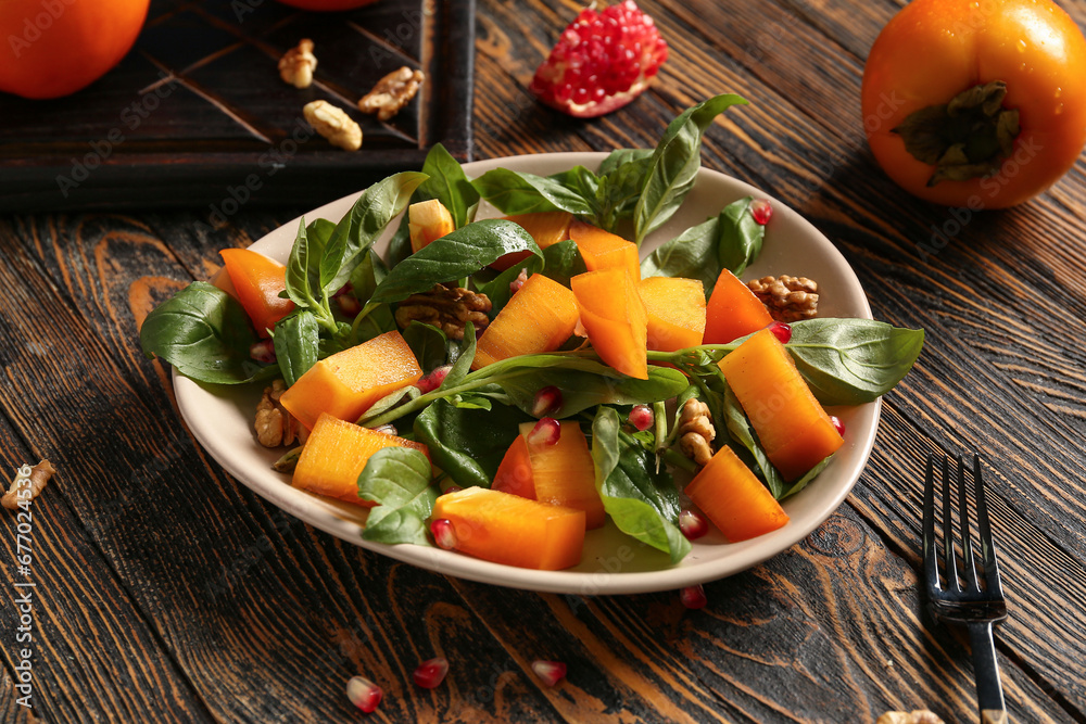 Bowl of delicious salad with persimmon, pomegranate seeds and walnut on wooden background