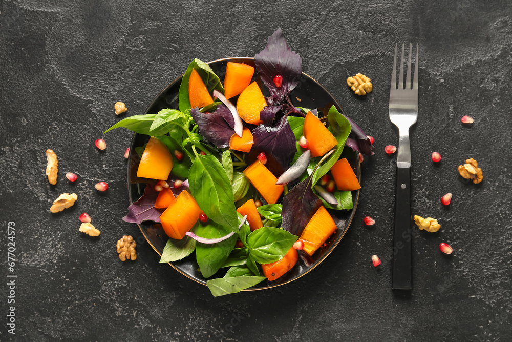 Plate of delicious salad with persimmon, onion and pomegranate seeds on black background