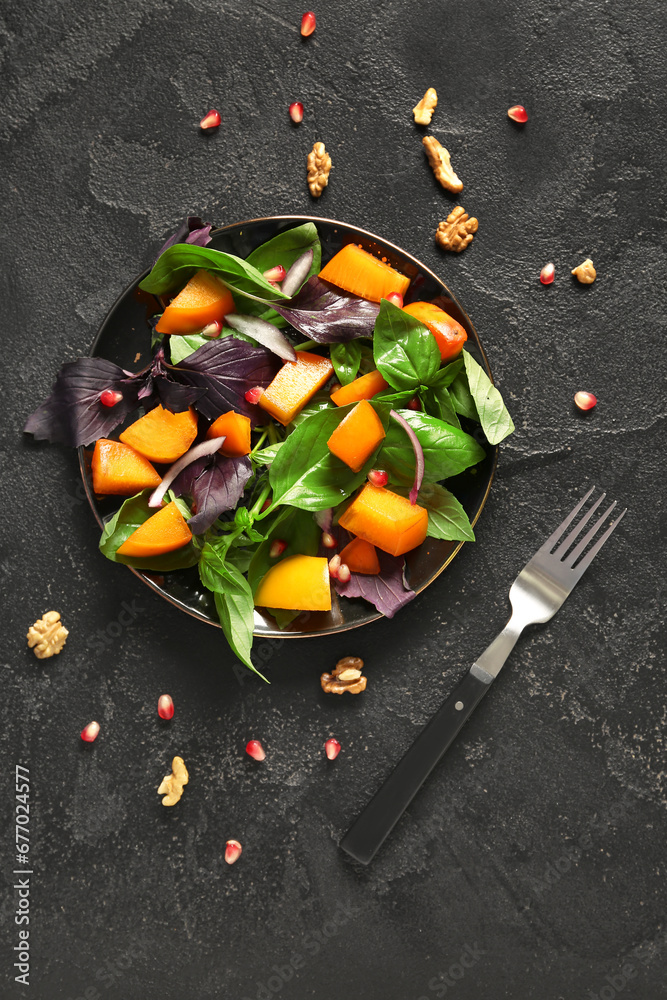 Plate of delicious salad with persimmon, onion and pomegranate seeds on black background