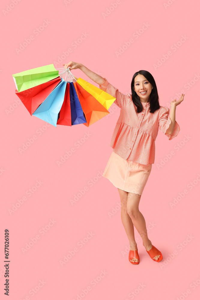 Young Asian woman with shopping bags on pink background