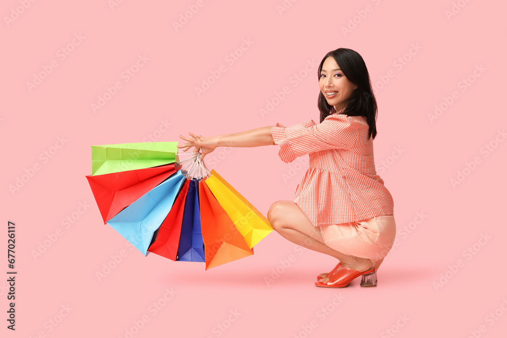 Young Asian woman with shopping bags on pink background