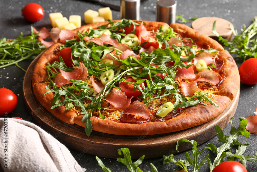 Wooden board of delicious pizza with tomatoes and arugula on black background