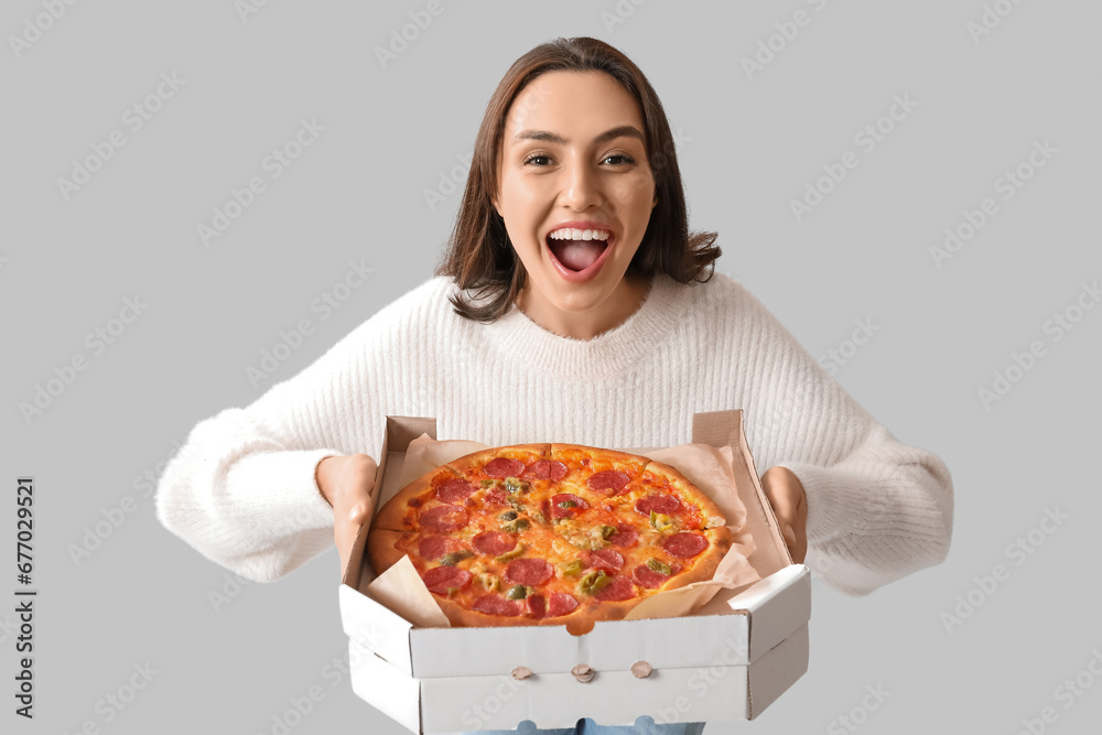 Young woman holding cardboard box with tasty pizza on white background