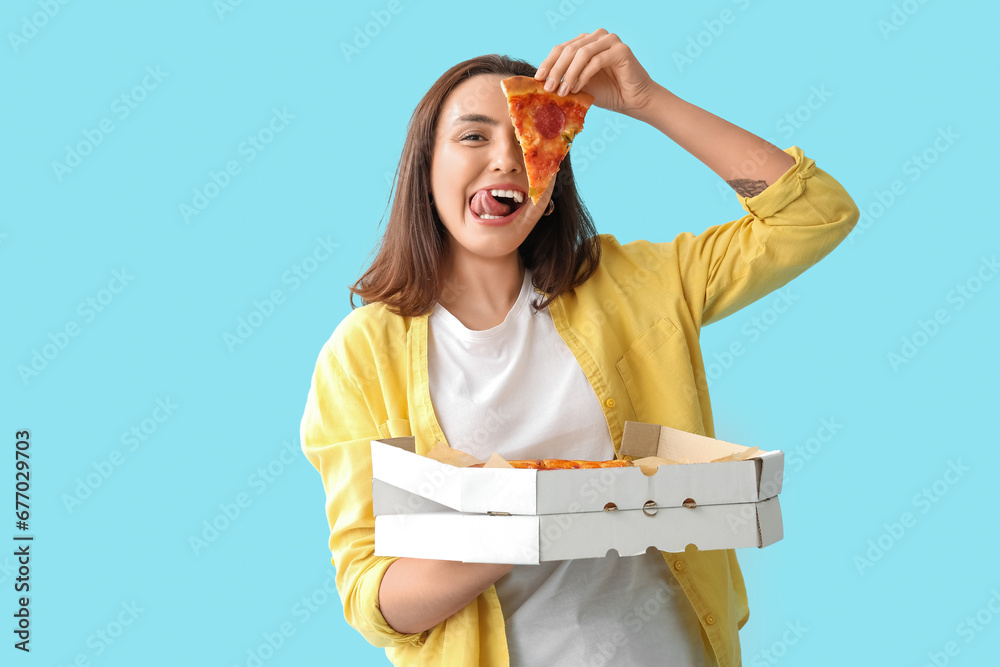 Young woman holding cardboard box with tasty pizza on blue background