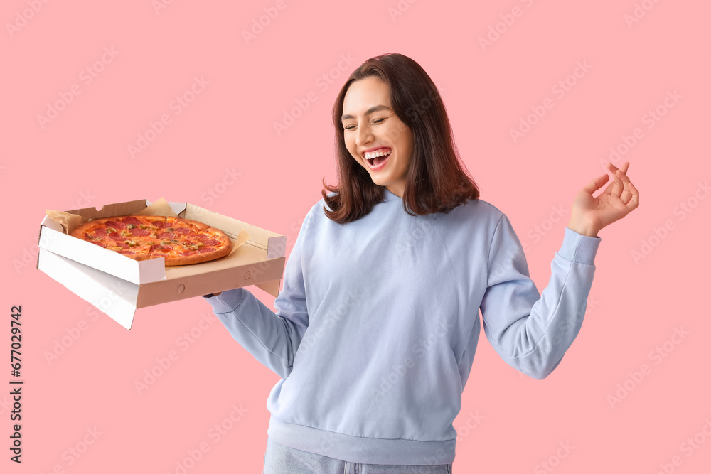 Happy young woman holding cardboard box with tasty pizza on pink background