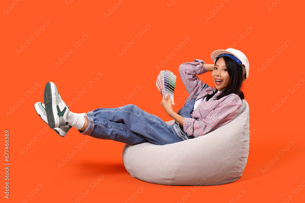 Young Asian woman with paint color palettes sitting on orange background