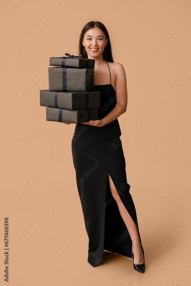 Beautiful young Asian woman with gift boxes on brown background. Black Friday sale