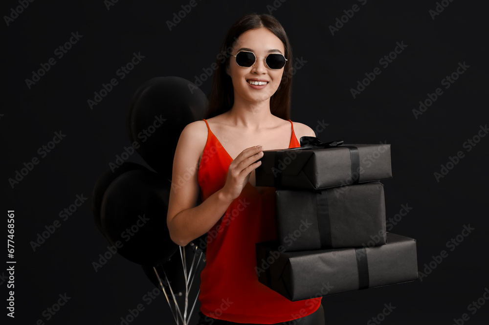 Beautiful young Asian woman with gift boxes and balloons on dark background. Black Friday sale