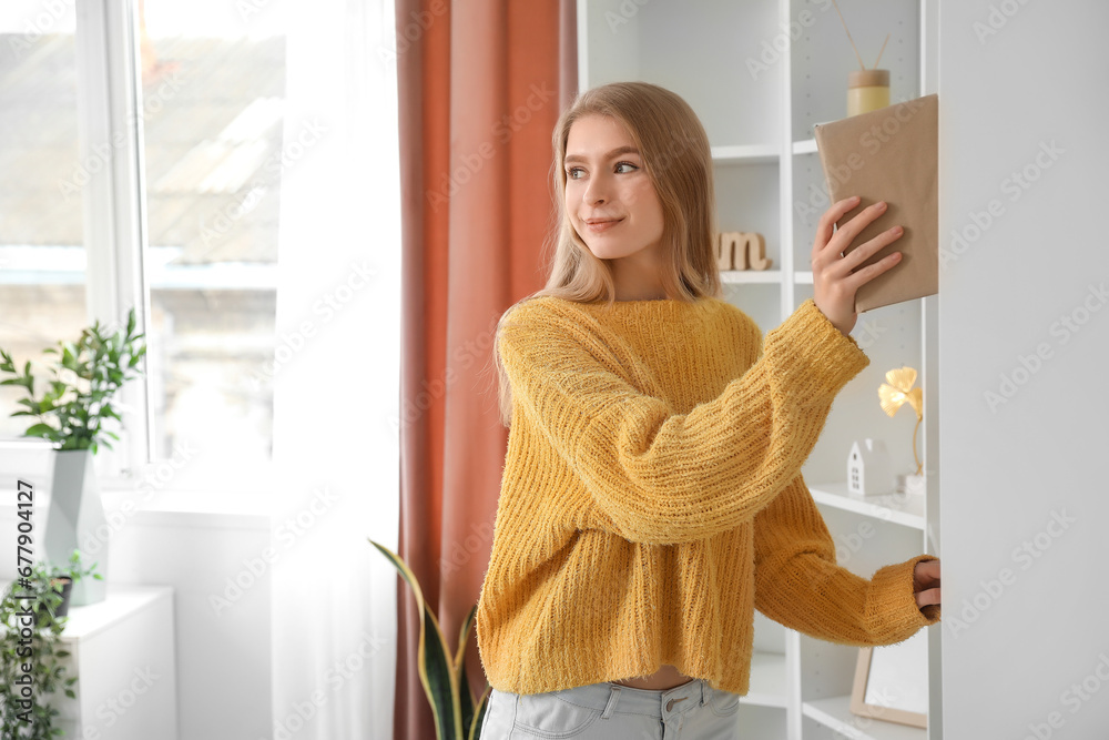 Young woman taking book from shelf at home