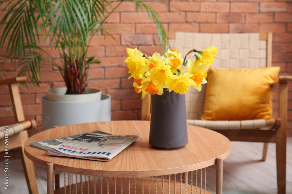 Vase with narcissus flowers and magazines on coffee table in living room