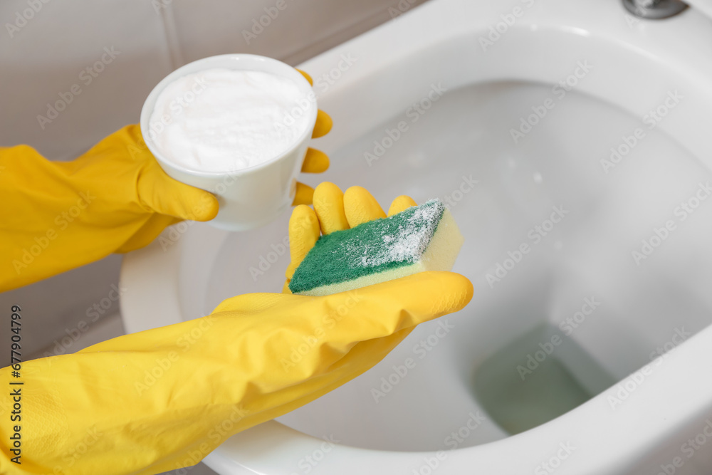 Woman in rubber gloves cleaning white toilet bowl with baking soda and sponge, closeup