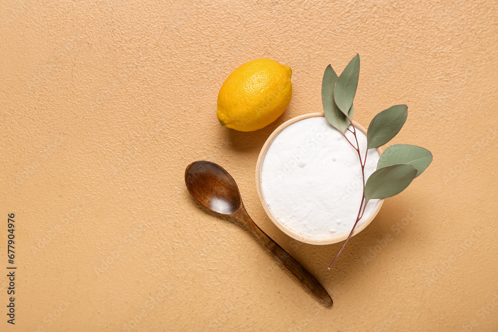 Bowl of baking soda, spoon, lemon and eucalyptus branch on color background