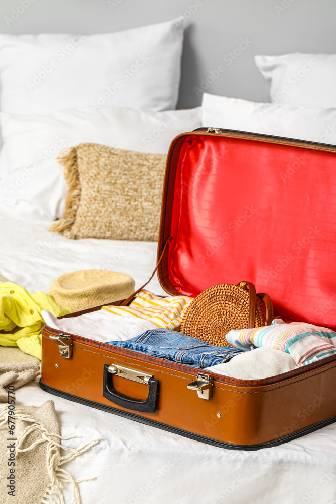 Open suitcase with female clothes on bed in room