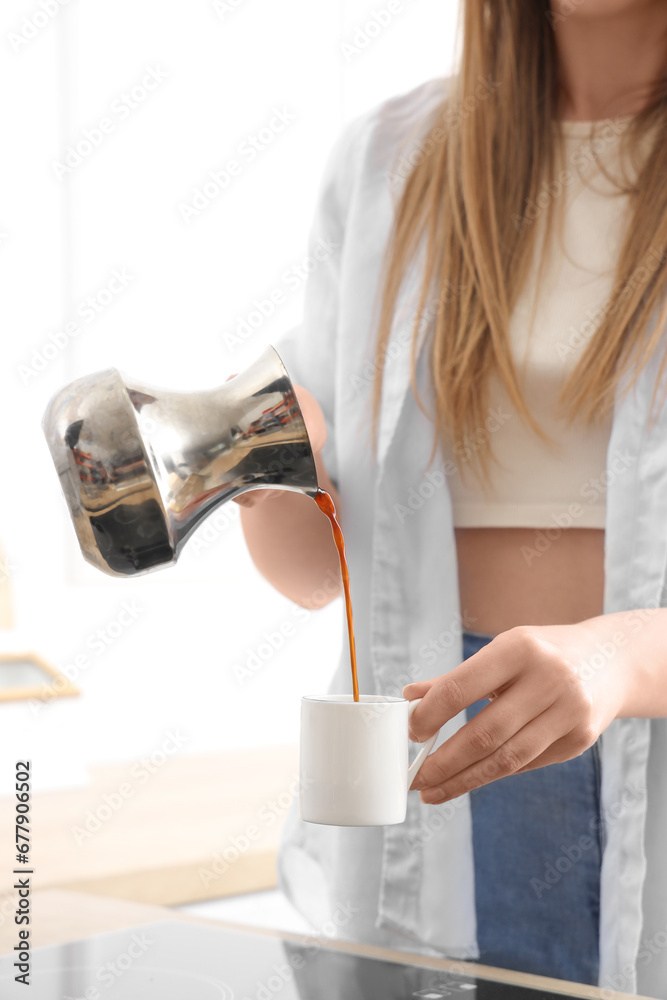 Woman pouring fresh coffee from jezve into cup in kitchen