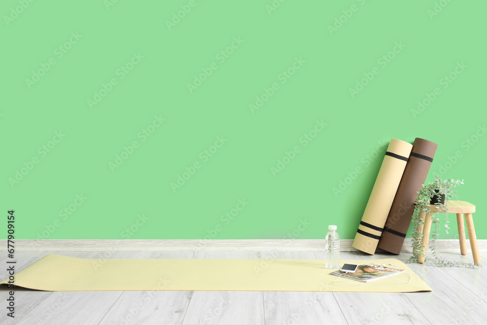 Fitness mats with mobile phone, magazine and stool near green wall in gym