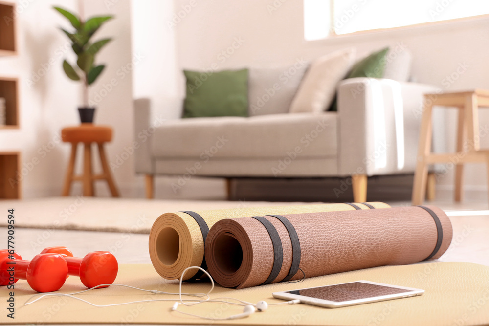 Tablet computer with earphones and dumbbells on fitness mat in living room