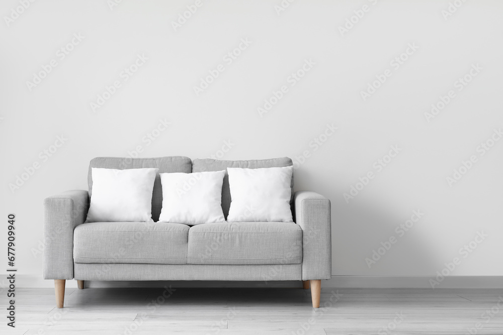 Grey sofa with pillows near white wall