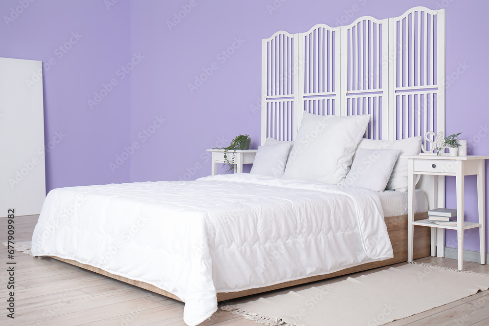 Interior of stylish bedroom with comfortable bed, white pillows, bedside tables and folding screen