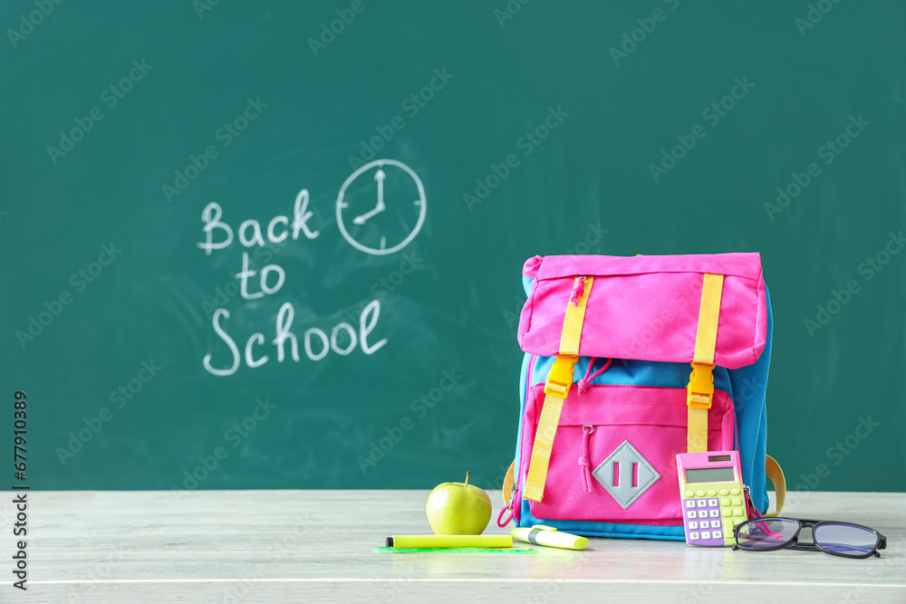 Backpack and supplies on table near green chalkboard with text BACK TO SCHOOL