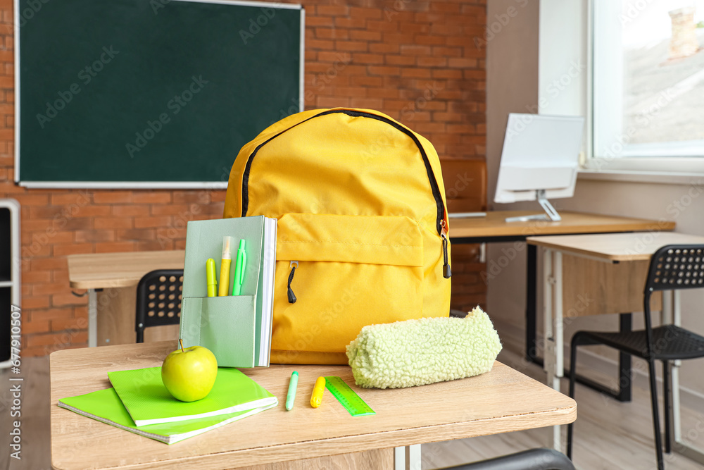 Yellow school backpack with stationery and fresh apple on desk in classroom