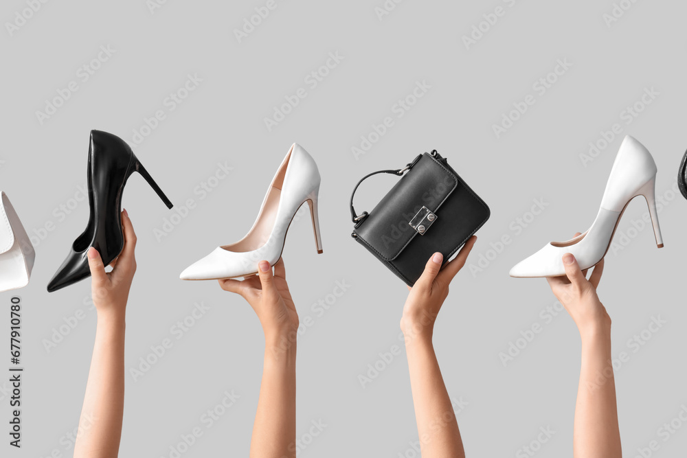 Female hands holding different stylish bags and high heels on grey background