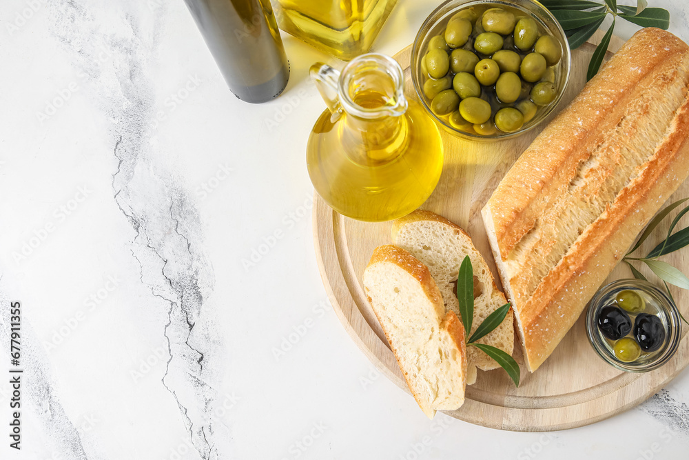 Wooden board with bread, olives and oil on white marble background