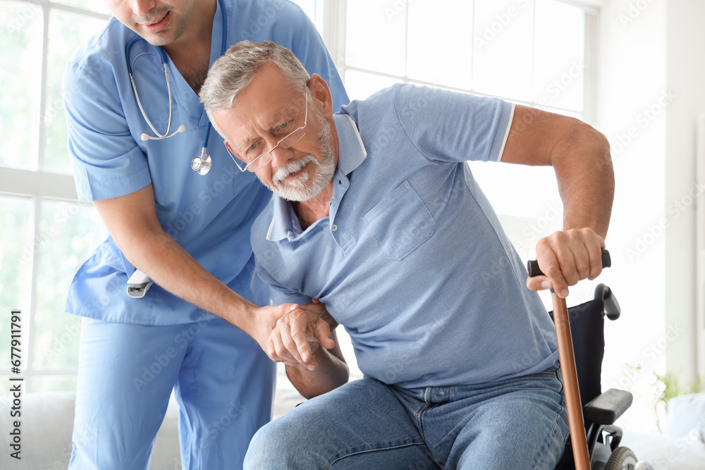 Male nurse helping senior man with stick to stand up at home