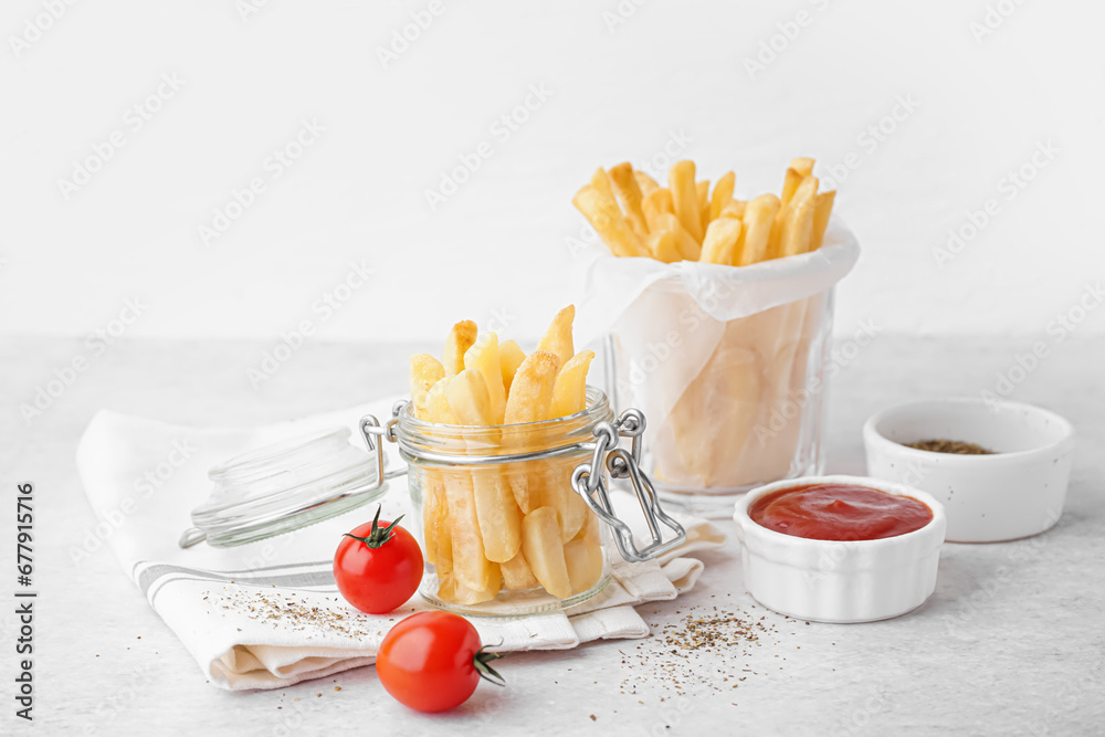 Jar and glass of tasty french fries with ketchup on white background