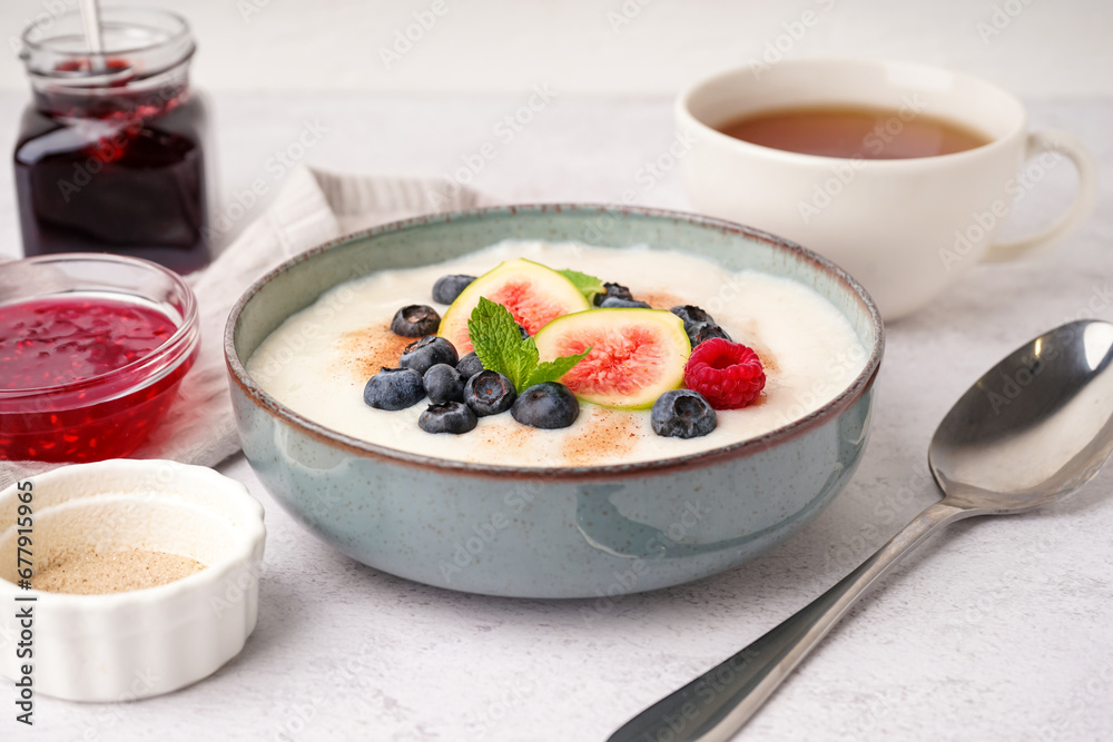 Bowl of tasty semolina porridge with fresh berries and figs on white background