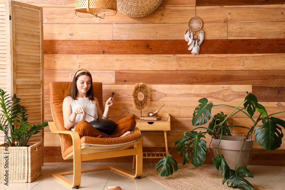 Young woman with sticks playing glucophone in armchair at home