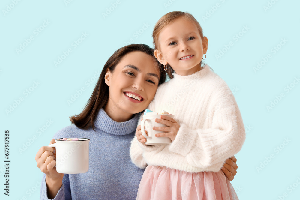 Young mother and her little daughter with mugs of hot chocolate on blue background