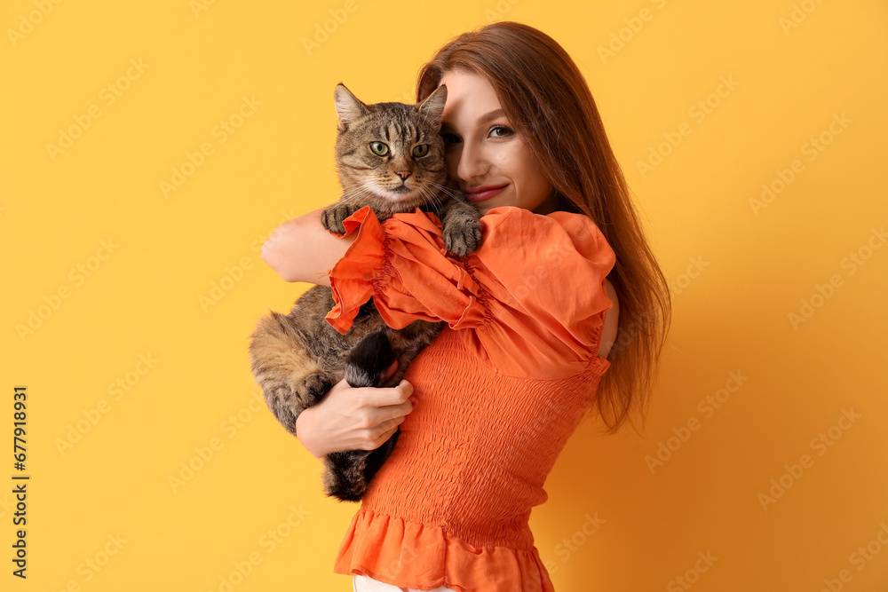 Pretty young woman with cute tabby cat on orange background