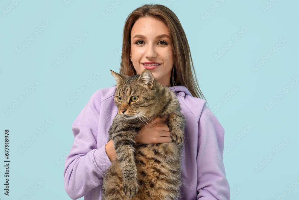 Pretty young woman with cute tabby cat on blue background