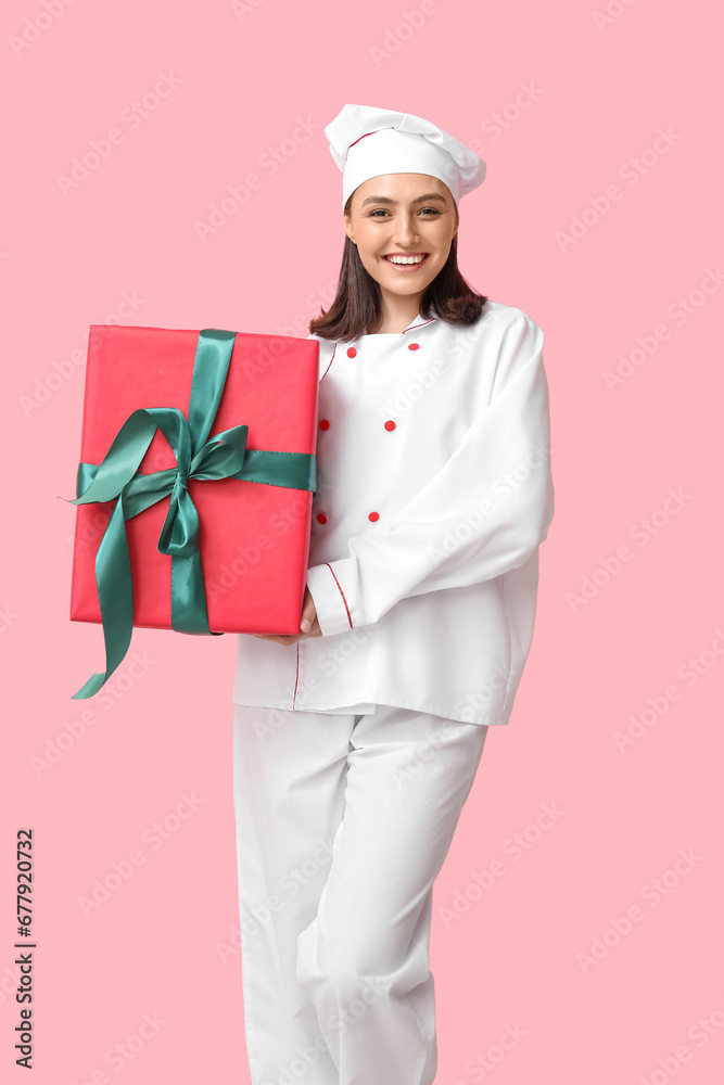 Beautiful female chef with gift box on pink background