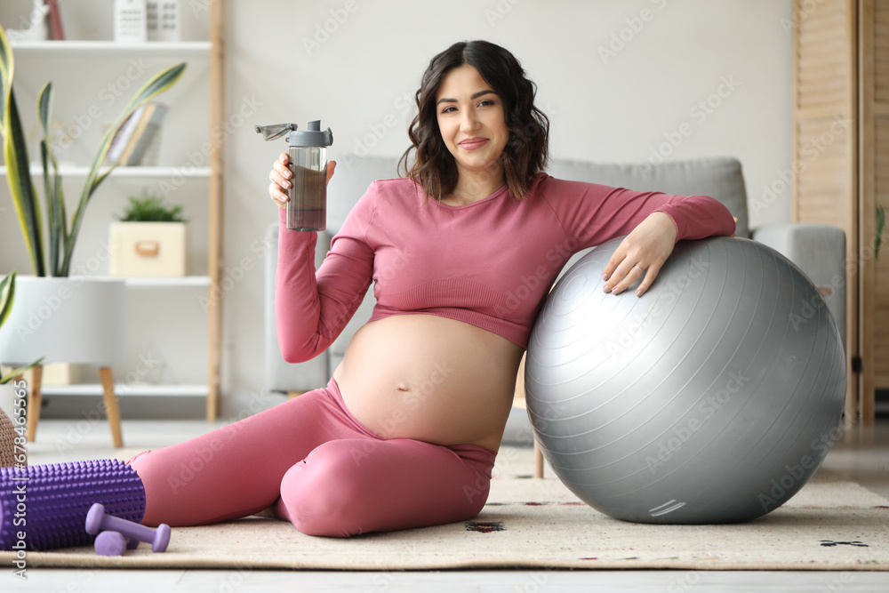 Sporty pregnant woman with bottle of water and fitball at home