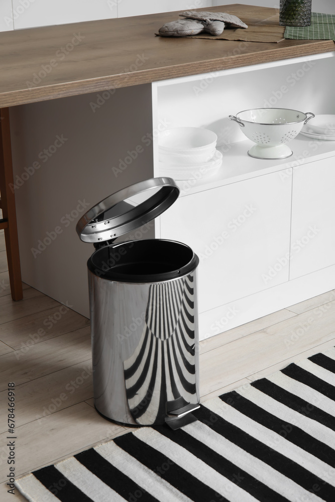 Opened metallic trash bin near table in interior of modern kitchen