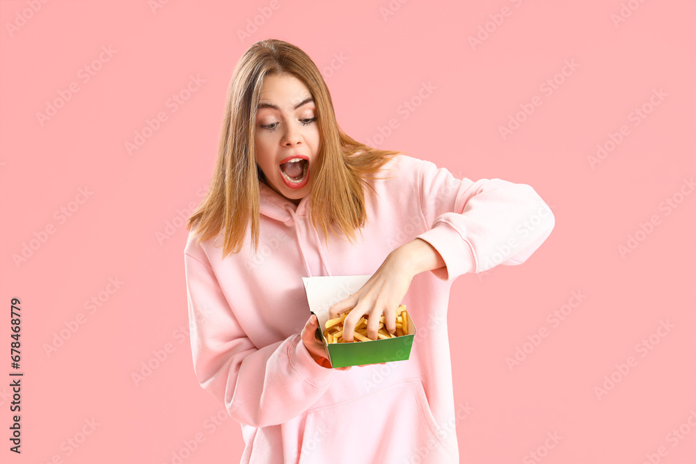 Beautiful shocked young woman with box of french fries on pink background