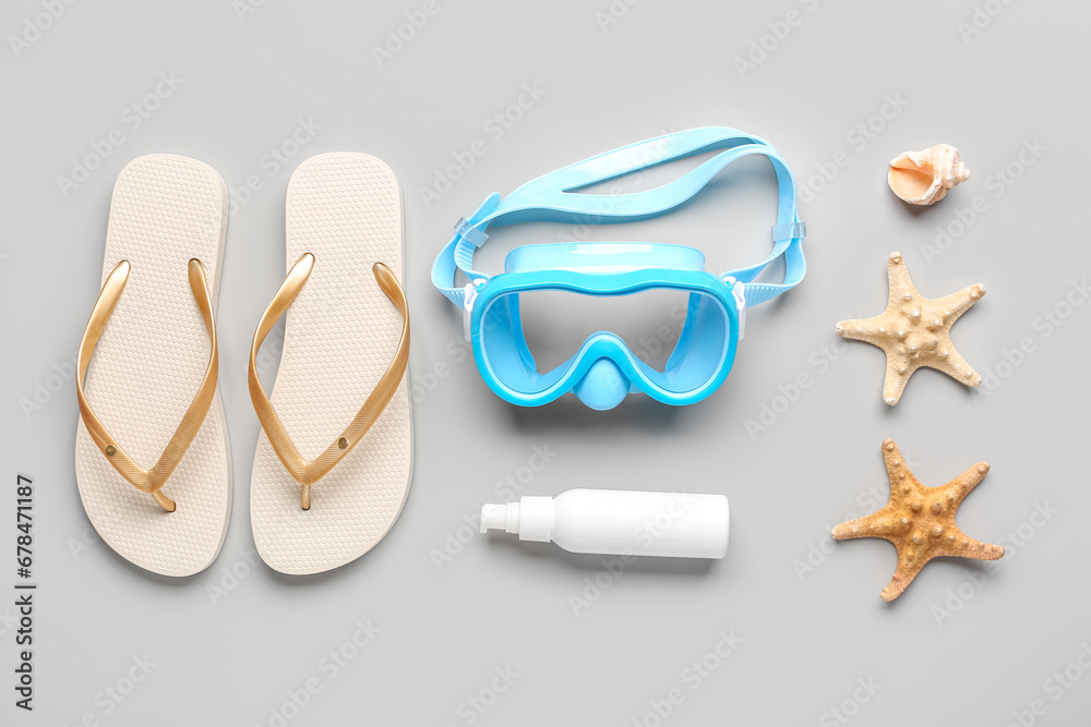 Composition with beach accessories and bottle of cosmetic product on grey background