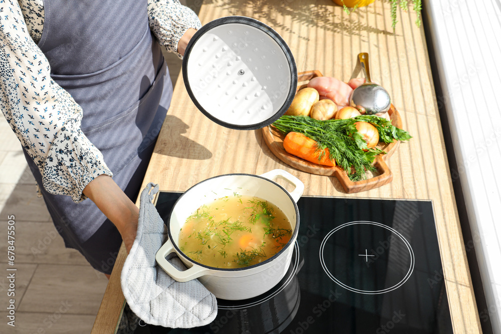 Young woman cooking chicken soup on stove in kitchen, closeup