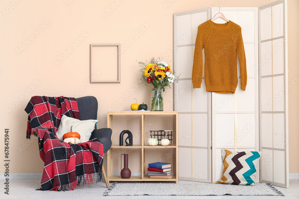 Interior of living room with autumn flowers on shelving unit, armchair and folding screen