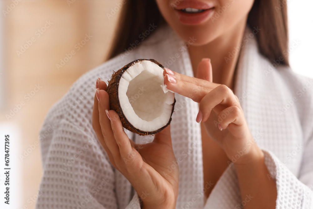 Beautiful young woman with coconut and oil in bathroom, closeup