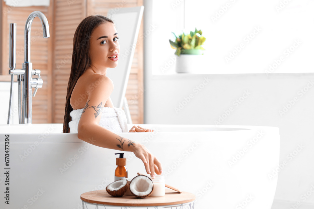 Beautiful young woman with coconut oil in bathroom