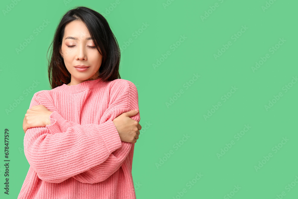 Young Asian woman hugging herself on green background