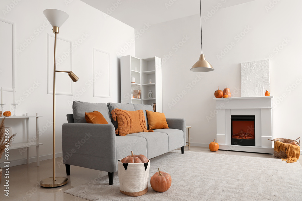 Autumn interior of living room with cozy grey sofa, fireplace and pumpkins