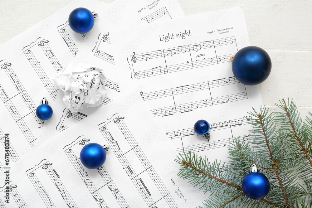 Music sheets, Christmas balls and fir branches on light wooden background, closeup