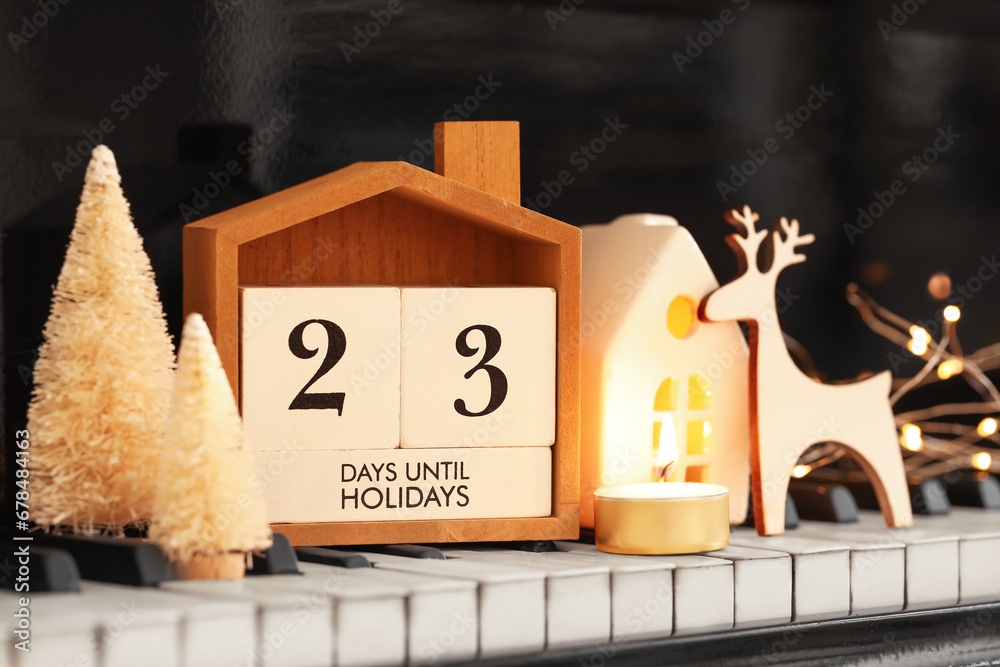 Calendar with text 23 DAYS UNTIL HOLIDAYS and Christmas decorations on piano keys, closeup