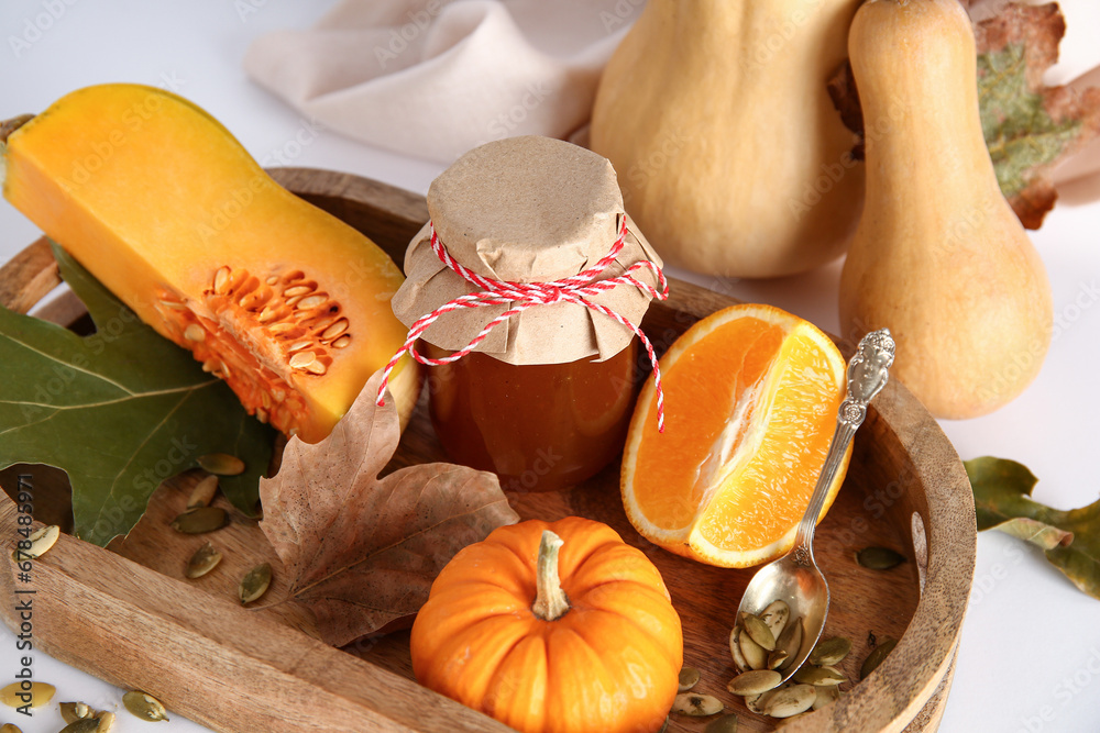 Jar of sweet pumpkin jam with orange and seeds on white background