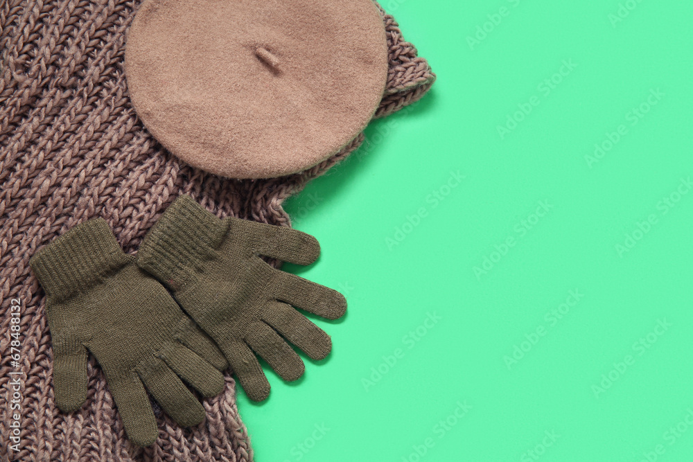 Warm gloves, beret and scarf on green background