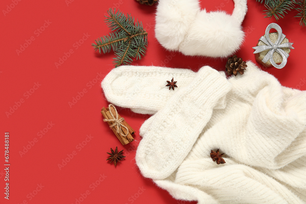 Composition with warm mittens, sweater, earmuffs and Christmas decor on red background